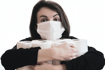 A woman in a medical face mask with armfuls of toilet paper rolls