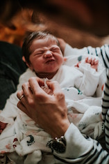 A very young baby lying on a lap; the adult's hand is holding one hand of the baby